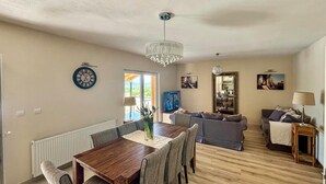 Amplia sala de estar con una mesa de comedor de madera, sofás grises, una araña y una televisión.