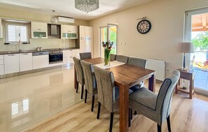 A modern kitchen with a dining area, a clock on the wall, and a view of the outdoors. - Stunning home in Sinj (Sinj)