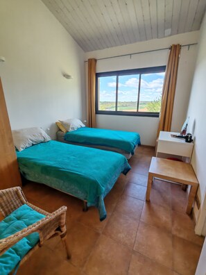 Ein Zimmer mit zwei Betten, einem Schreibtisch, einem Stuhl und einem Fenster mit Blick auf die Landschaft.