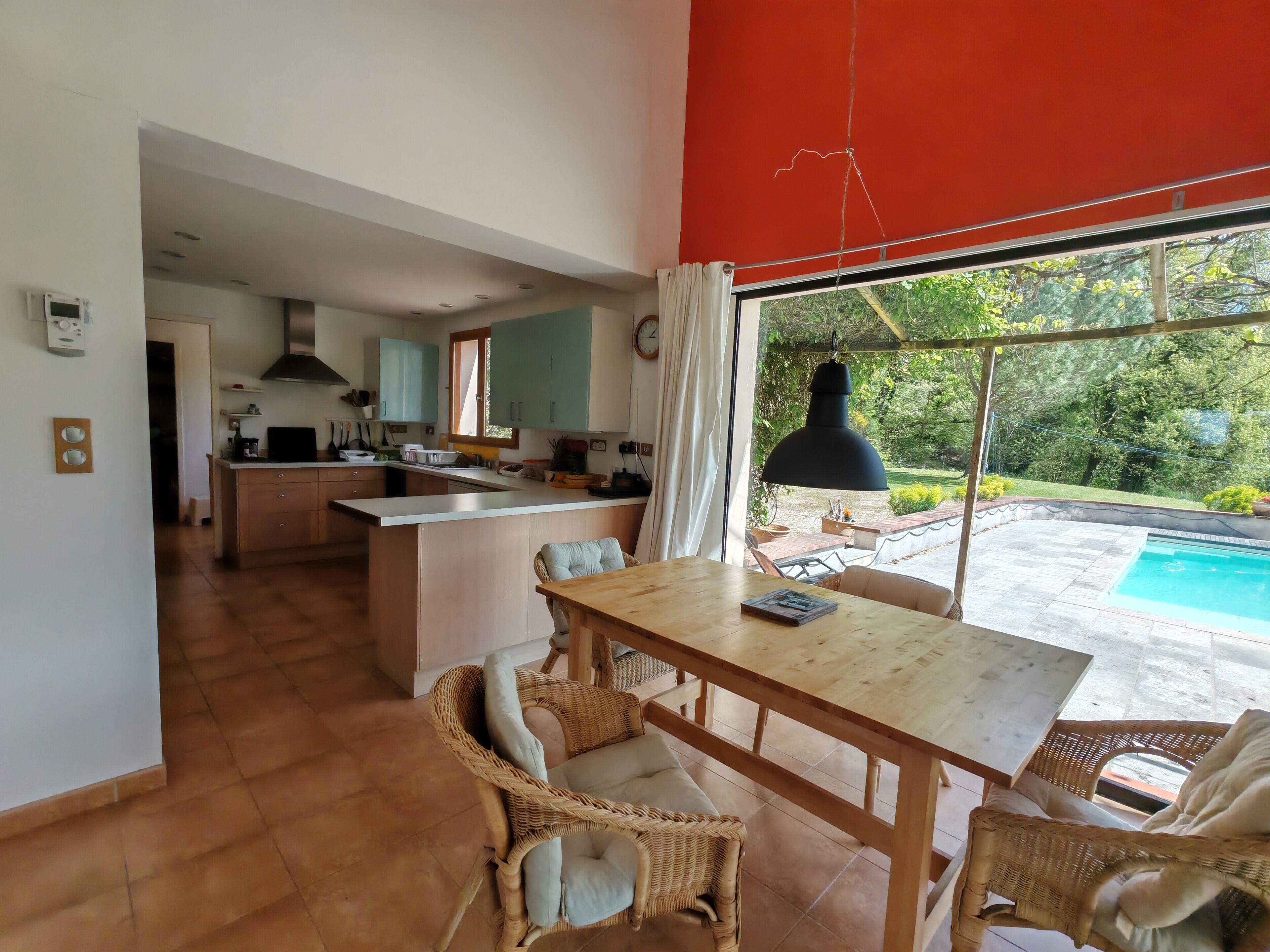 A modern kitchen with a central island, a dining area with wicker chairs, and a view of a swimming pool.
