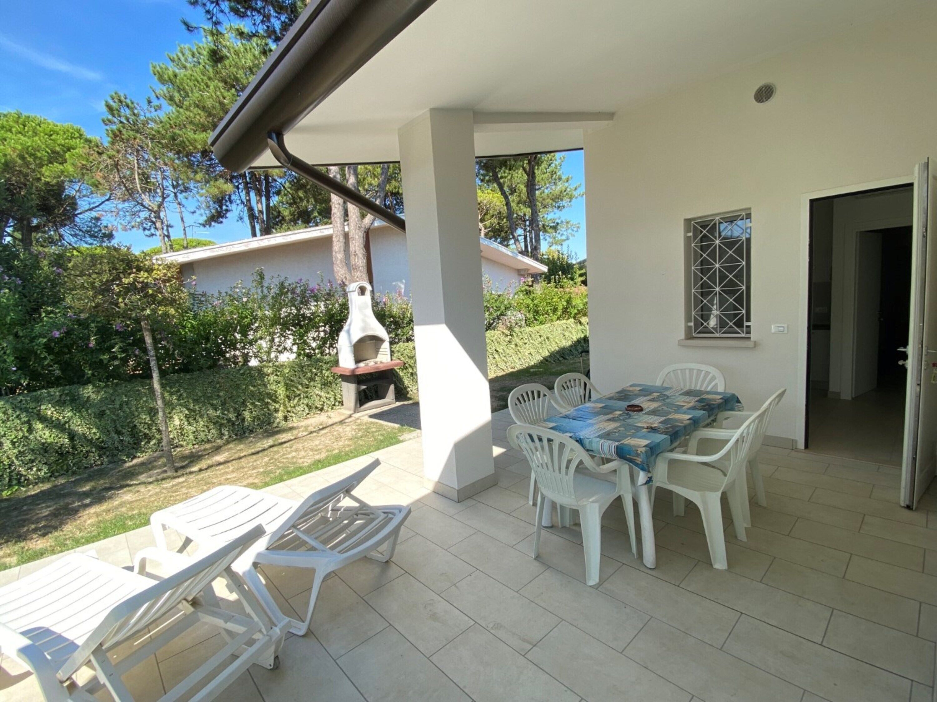 A covered patio with a table and chairs, a barbecue grill, and a view of the surrounding greenery.