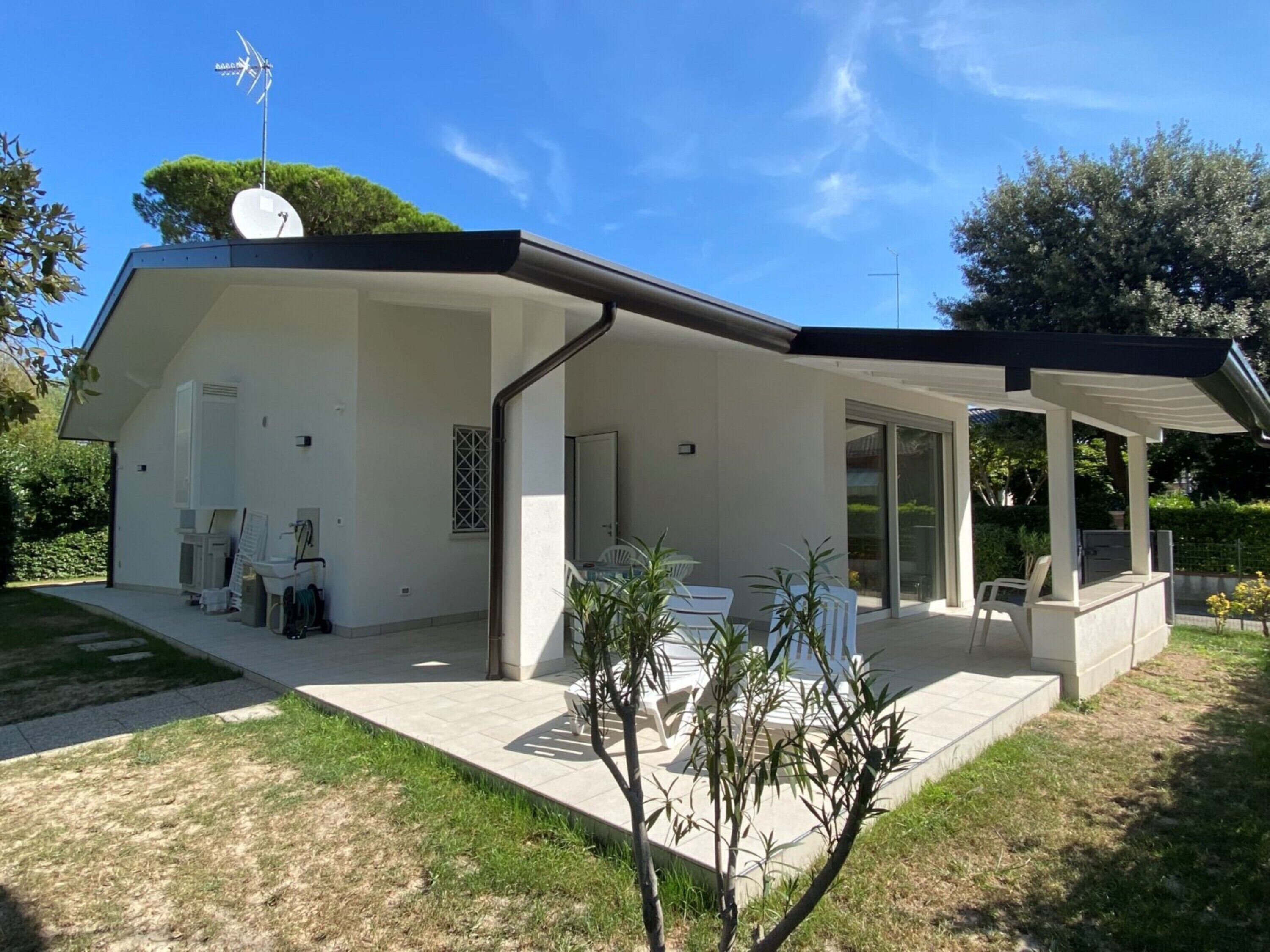 Una casa moderna con un porche cubierto, una antena parabólica y un pequeño jardín.