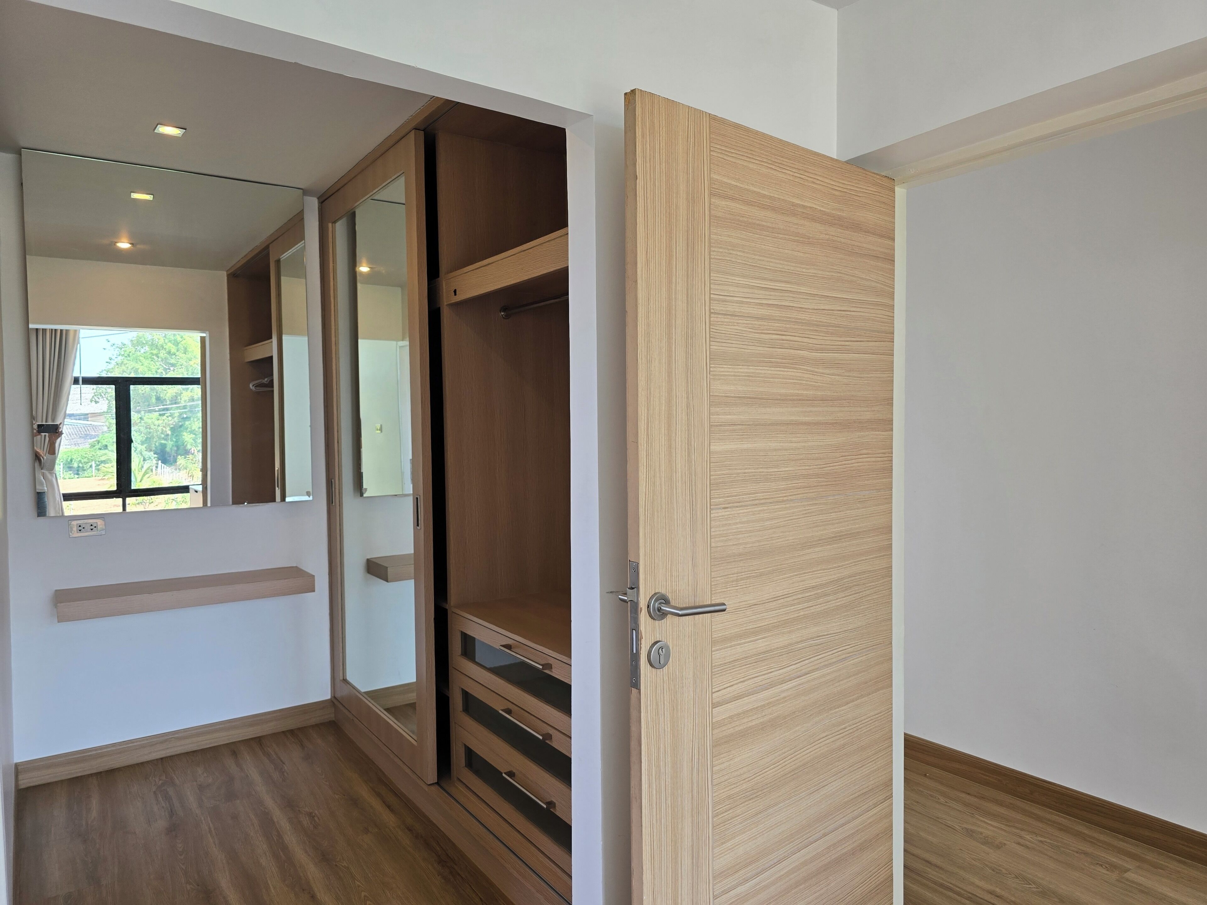 Ein Zimmer mit Holztür, Spiegel, Fenster und Holzboden.