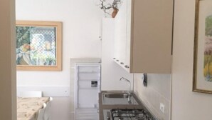Een compacte keuken met een gasfornuis, een spoelbak en een klein aanrecht. Er is een eethoek met een tafel en stoelen zichtbaar op de achtergrond.