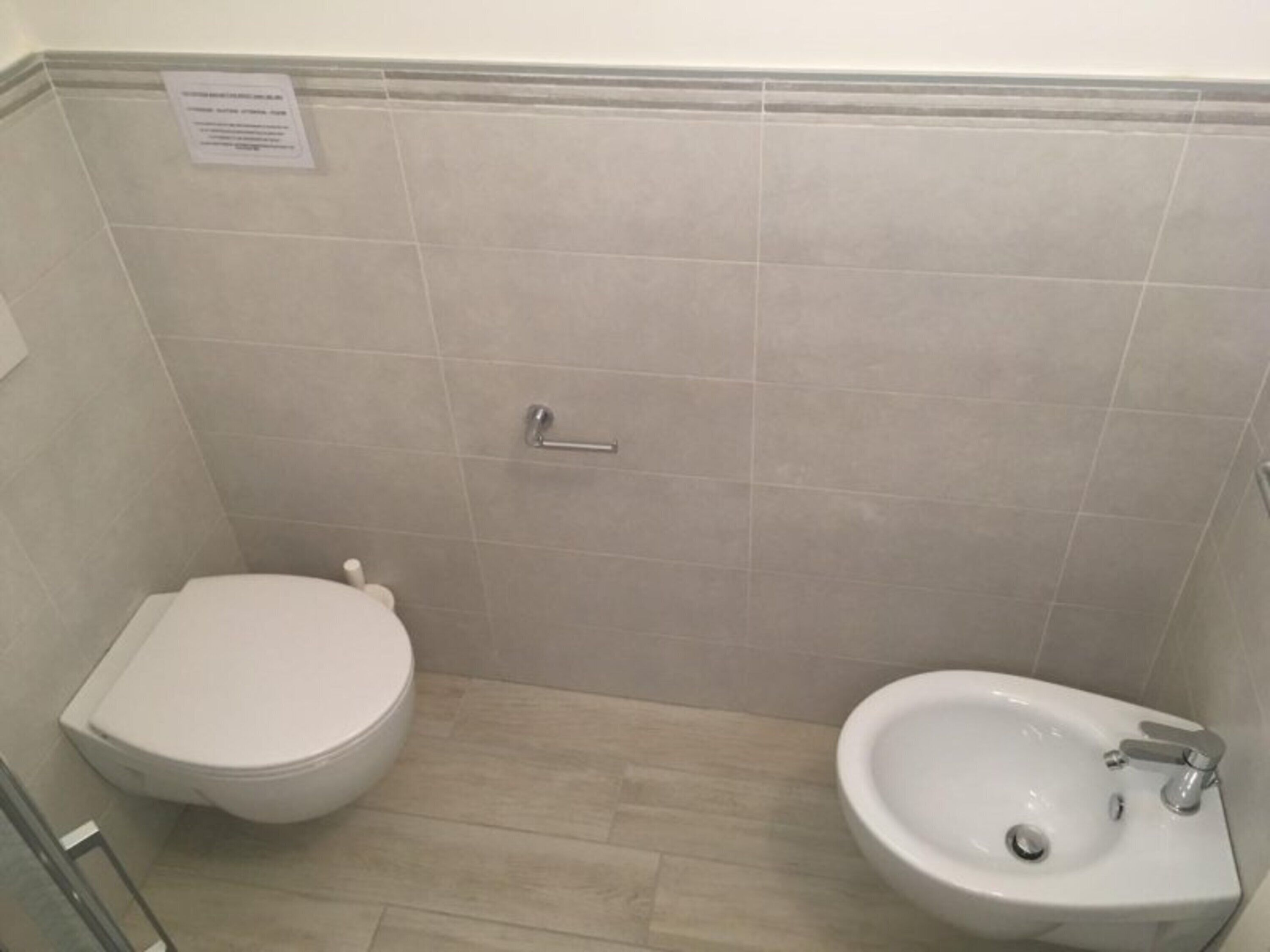 A bathroom with a toilet, bidet, and a handrail.
