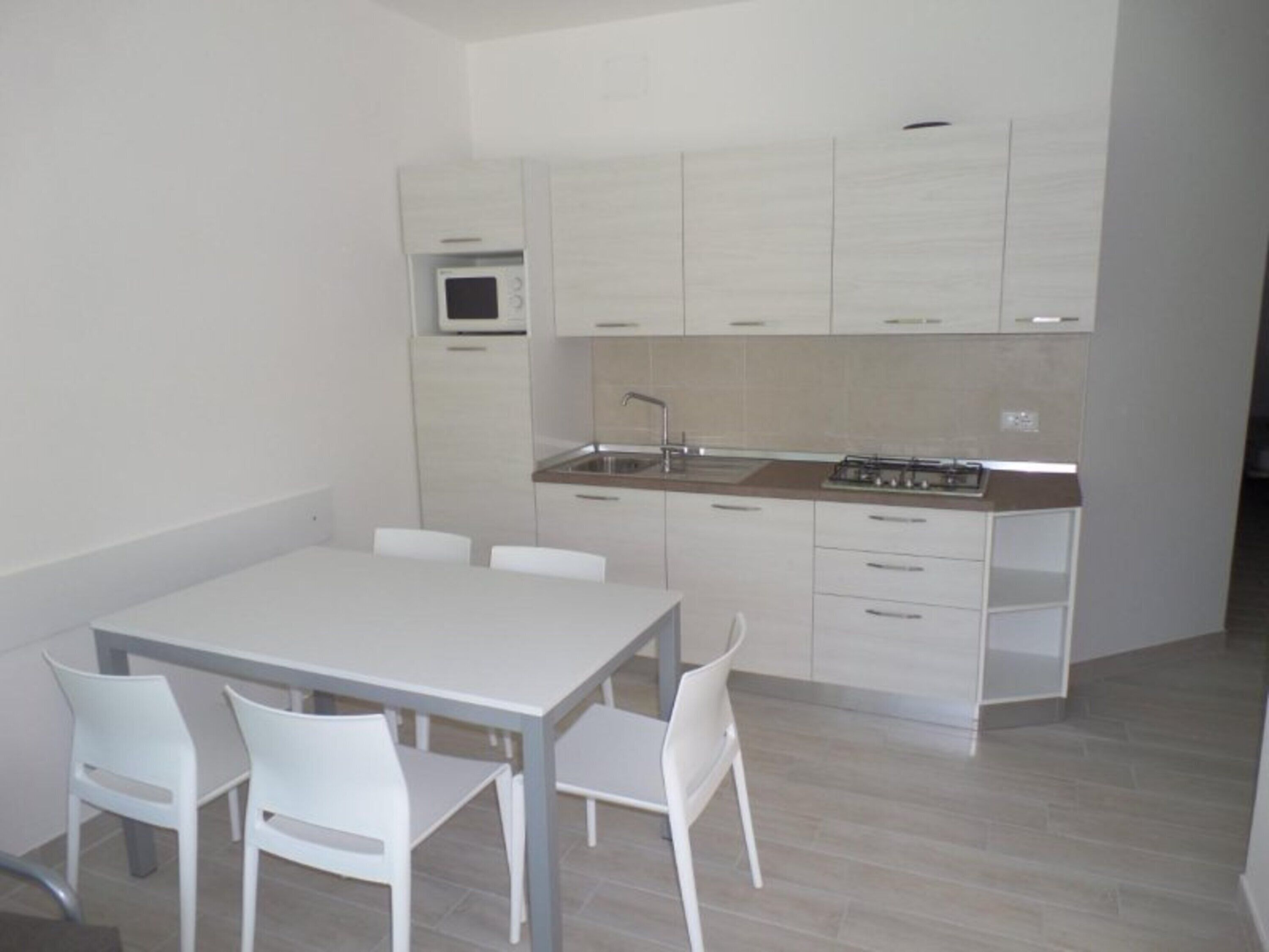 Een moderne keuken met witte kasten, een magnetron, een spoelbak en een fornuis. Er staat een eettafel met vier stoelen.