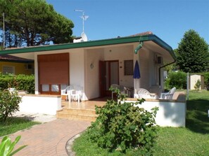 Einbungalow mit überdachter Veranda, Satellitenschüssel und kleinem Garten.