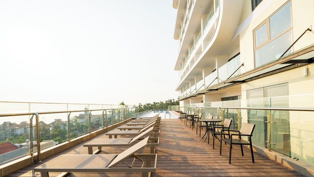 Um terraço com espreguiçadeiras e mesas, guarda-corpos de vidro e vista para a cidade.