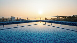 Piscina com azulejos e vista para o céu e edifícios ao longe.