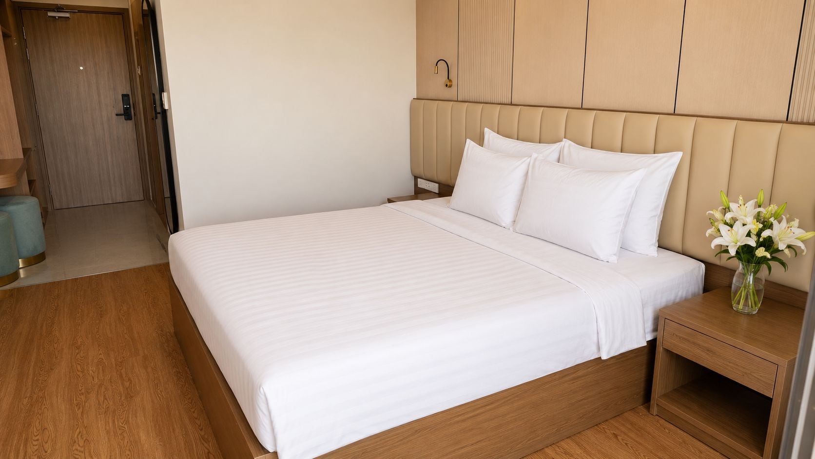 Habitación de hotel con una cama grande, cabecera de madera, mesita de noche con un florero y suelo de madera.