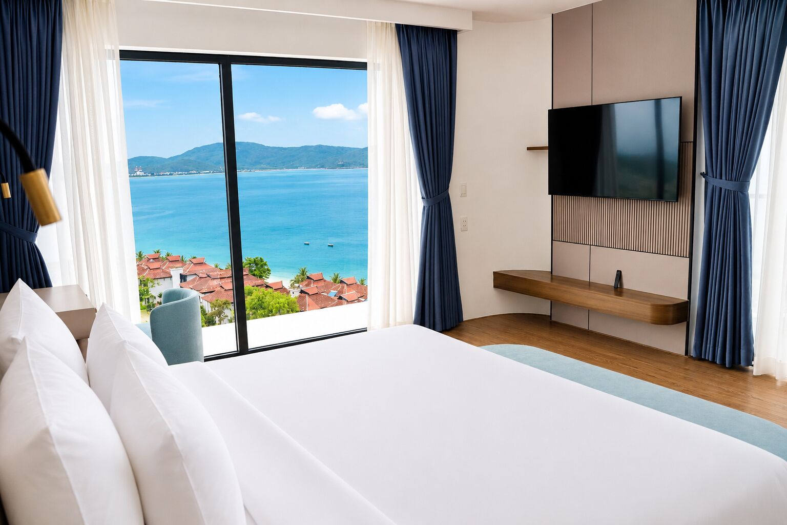 A hotel room with a large bed, a TV mounted on the wall, a wooden bedside table, and a view of the sea and mountains.