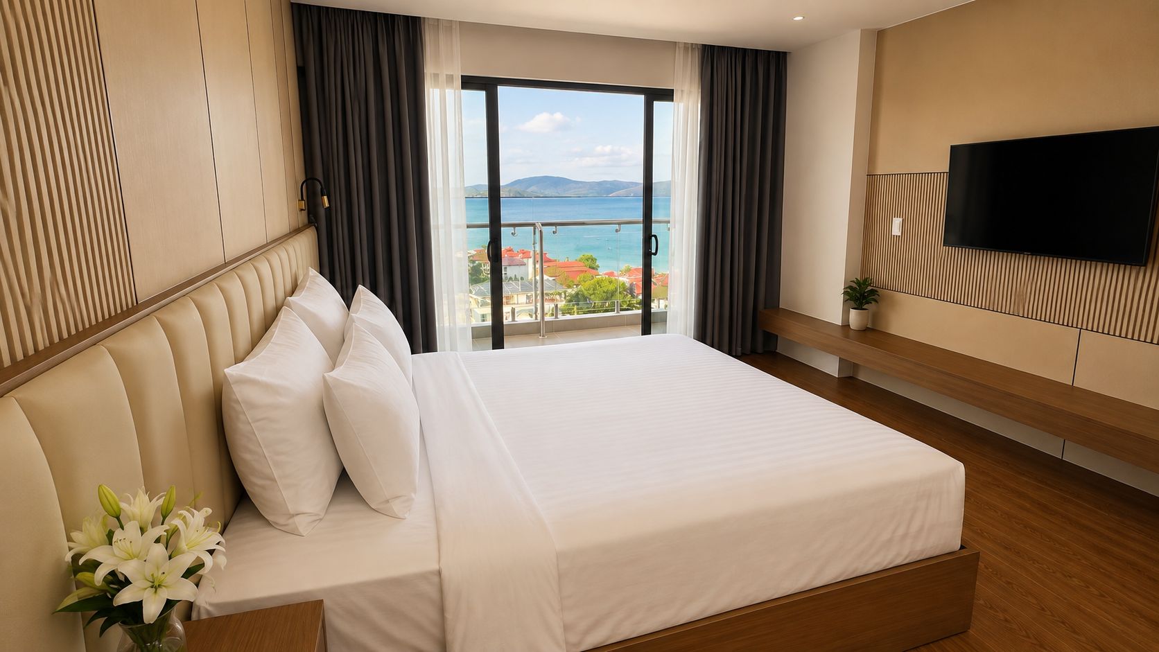 A hotel room with a large bed, a TV, and a balcony with a view of the sea.