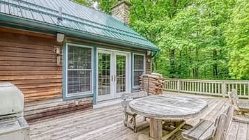 Une terrasse en bois avec une table ronde et des bancs, un toit en métal et une rambarde blanche.