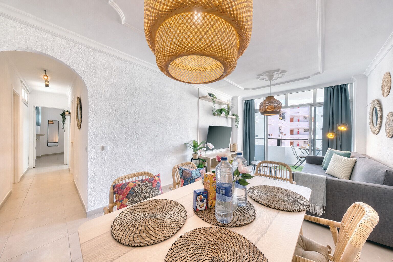 Un salon moderne comprenant un coin repas, des meubles en osier et une grande fenêtre agrémentée de rideaux.