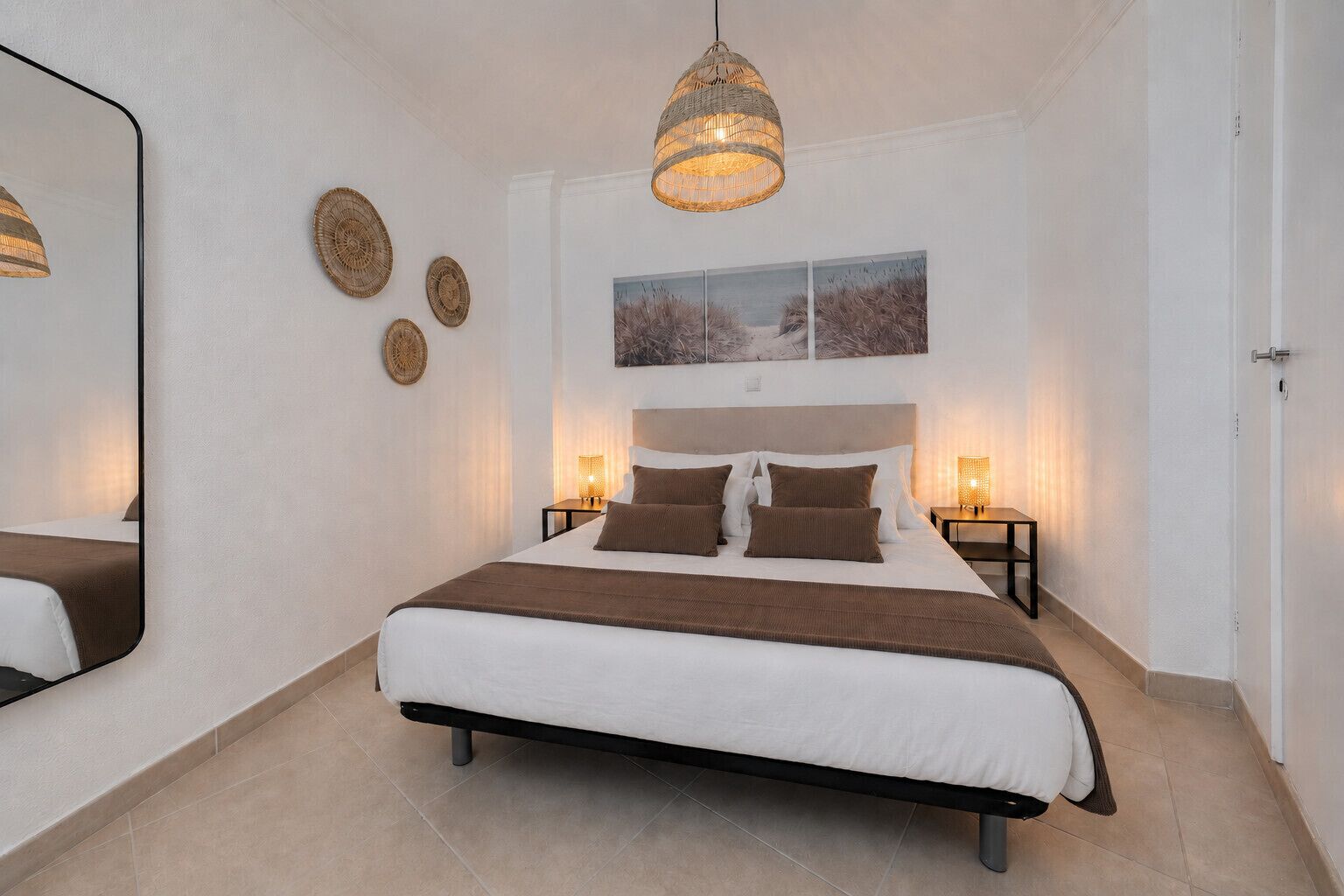 Ein Schlafzimmer mit einem großen Bett, Nachttischlampen, einer Hängeleuchte und Wandbildern.