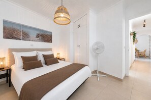 Ein Schlafzimmer mit Bett, Nachttischlampen, einem Standventilator und Kunstwerken an der Wand.