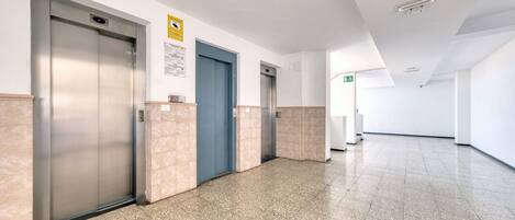 Un pasillo limpio y moderno con dos ascensores, una puerta azul y una pared blanca con un letrero amarillo.