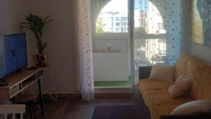 Una sala de estar con sofá, televisión, escritorio y planta en maceta.