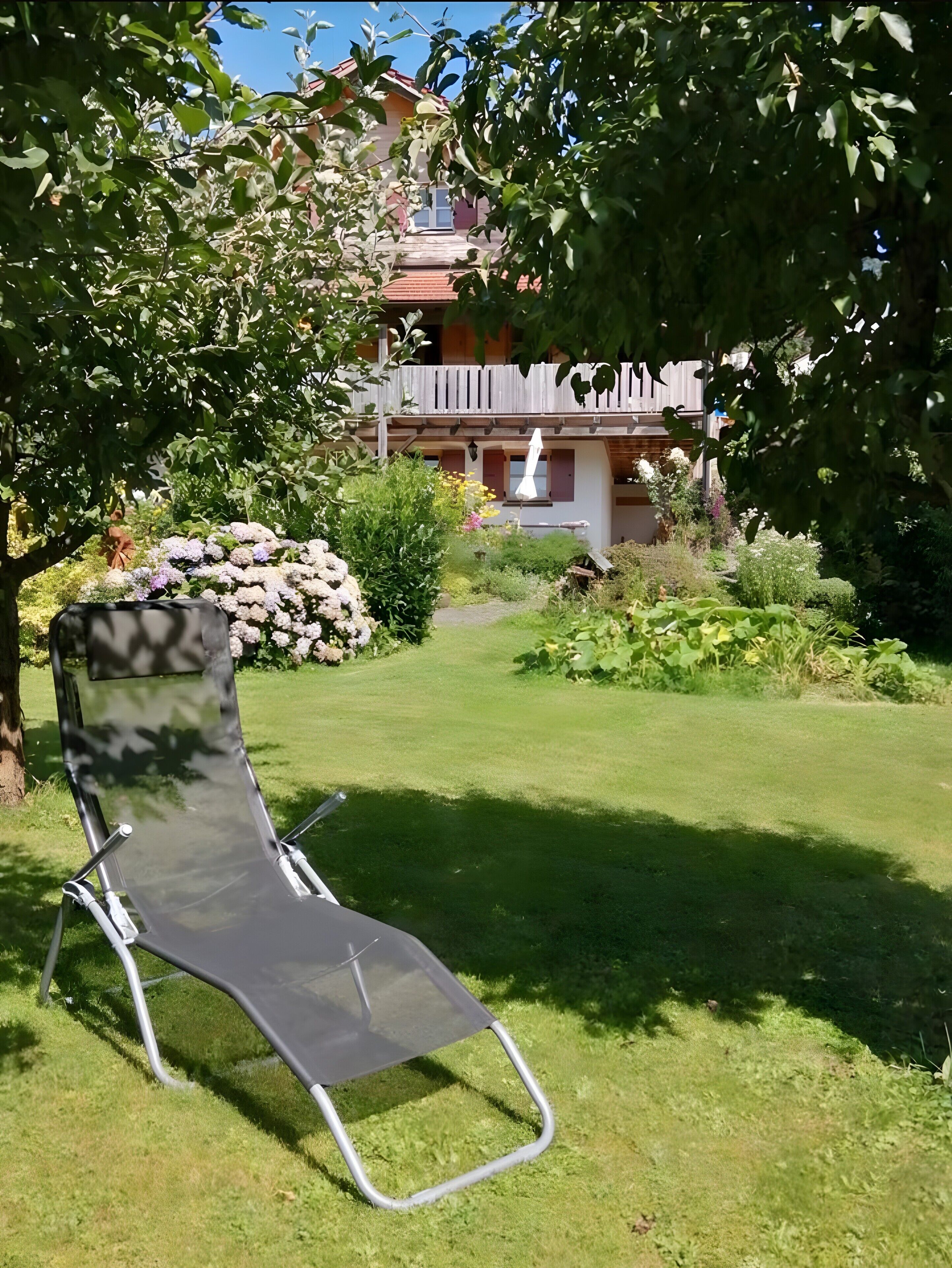 Un jardin avec une pelouse, une clôture en bois et un bâtiment doté d’un balcon.