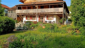 A two-story wooden house with a balcony, surrounded by a garden with various plants and flowers. - Landblick Lalling Apartment with Private Terrace, Garden, and Wi-Fi (Lalling)