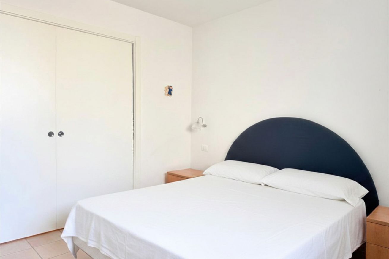Un dormitorio con una cama, una mesita de noche, un armario blanco y una puerta.