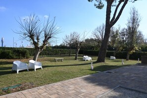 A paved outdoor area with white chairs and a bench, surrounded by trees and a hedge. - M466 - Marcelli, three-room apartment  (Marcelli)