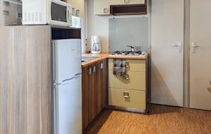 A compact kitchen with a refrigerator, microwave, coffee maker, gas stove, and wooden cabinets. - Cozy (sta)caravan in Aureilhan (Aureilhan)