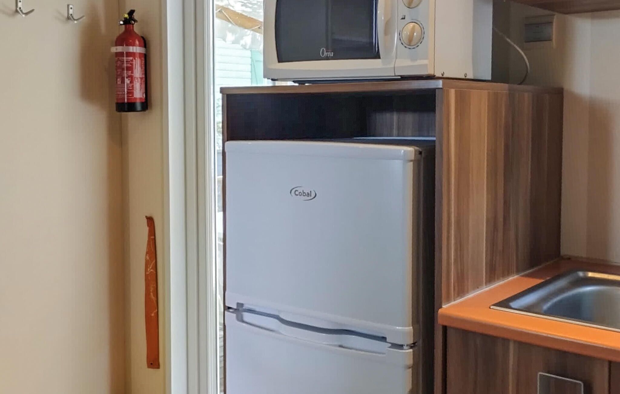 A kitchen with a Cobal refrigerator, a microwave, and a fire extinguisher on the wall.