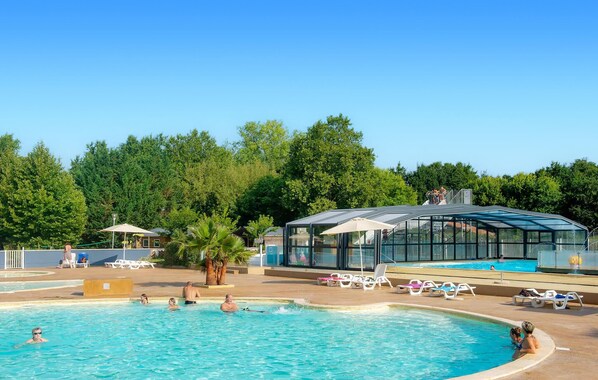 A swimming pool with lounge chairs, a glass-enclosed structure, and trees in the background. - Cozy (sta)caravan in Aureilhan (Aureilhan)