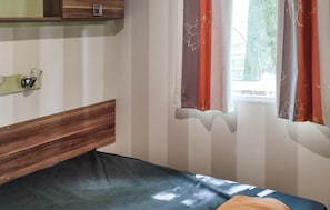 A room with a bed, a wooden headboard, a window with curtains, and a wall-mounted shelf. - Cozy (sta)caravan in Aureilhan (Aureilhan)