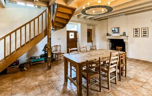 A spacious room with a wooden staircase, a dining table with chairs, a fireplace, and a dartboard. - Cottage à la campagne (Mérigny)