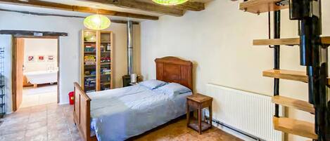 Un dormitorio con una cama de madera, una mesita de noche, un radiador, una escalera de madera y un baño visible a través de una puerta abierta.