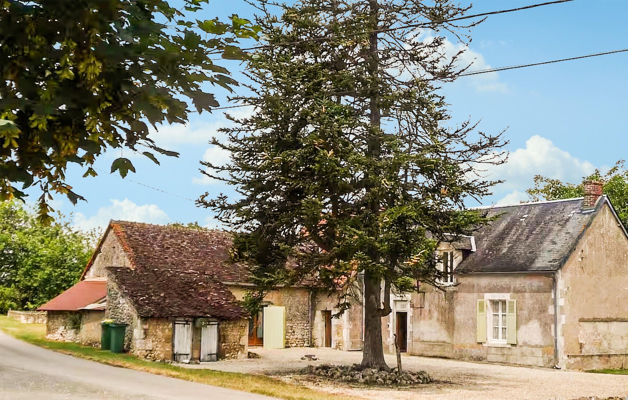 A rustic stone building with a sloped roof, a tree in front, and a clear sky.