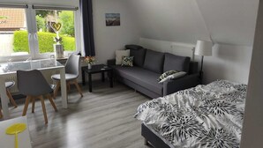 A modern hotel room with a dining area, a sofa, a bed with a patterned bedspread, a lamp, and a view of greenery outside. - Relax under thatch with pool, beach chairs and loungers (Belum)