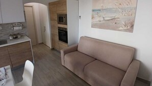 A compact living space with a kitchenette, a sofa, and a painting on the wall. - Vacation home (Isola Rossa)