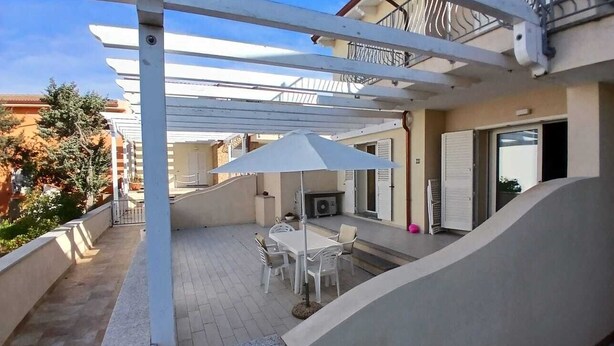 A covered patio with a table and chairs, a white umbrella, and a white railing. - Vacation home (Isola Rossa)