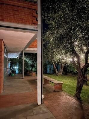 A covered outdoor area with a brick wall, a bench, and a tree illuminated by lights.