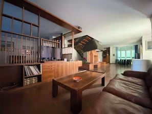 Amplia sala de estar con una mesa de centro de madera, un sofá de cuero marrón y una escalera que lleva a un nivel superior.