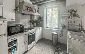 A kitchen with a microwave, stove, oven, and sink. There is a window with a view of greenery outside. - Charmante maison cosy (La Brosse-Montceaux)
