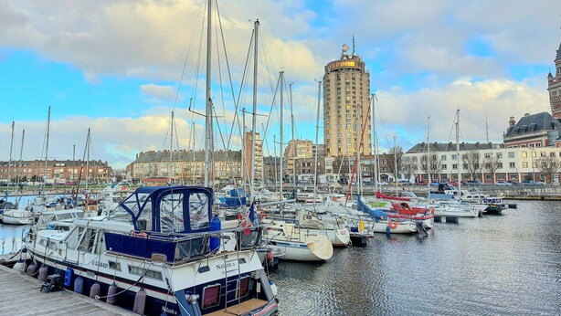 A marina with multiple boats docked, a tall building in the background, and a clear sky. - Gorgeous apartment in Grand-Fort-Philippe (Grand-Fort-Philippe)