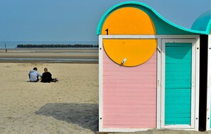 Un cabanon de plage à l’extérieur rose et turquoise, doté d’une fenêtre ronde et d’une porte.