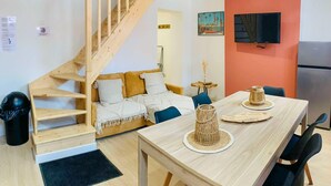 A modern apartment with a wooden staircase, a sofa with a white blanket, a dining table with a woven centerpiece, and a TV mounted on the orange wall. - Gorgeous apartment in Grand-Fort-Philippe (Grand-Fort-Philippe)