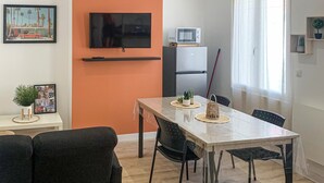 A modern living room with a dining table, black chairs, a flat-screen TV, a microwave, and a refrigerator. - Gorgeous apartment in Grand-Fort-Philippe (Grand-Fort-Philippe)