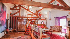 Ein rustikaler Raum mit sichtbaren Holzbalken, einer Treppe, einer Couch, einem Tisch und einem gemusterten Teppich.