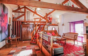 Ein rustikaler Raum mit sichtbaren Holzbalken, einer Treppe, einer Couch, einem Tisch und einem gemusterten Teppich.