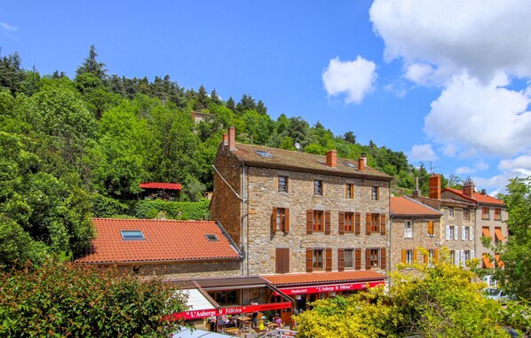 Ein Gebäude aus Stein mit rotem Ziegeldach, ein Café mit Außenbereich und üppiges Grün im Hintergrund.