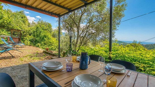 Un espace de restauration en plein air avec une table dressée pour quatre personnes, entouré d’une végétation luxuriante et offrant une vue dégagée sur le paysage.