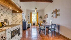 Une cuisine avec un mur recouvert de carreaux, un plafond avec poutres apparentes et un coin repas comprenant des chaises et une table.