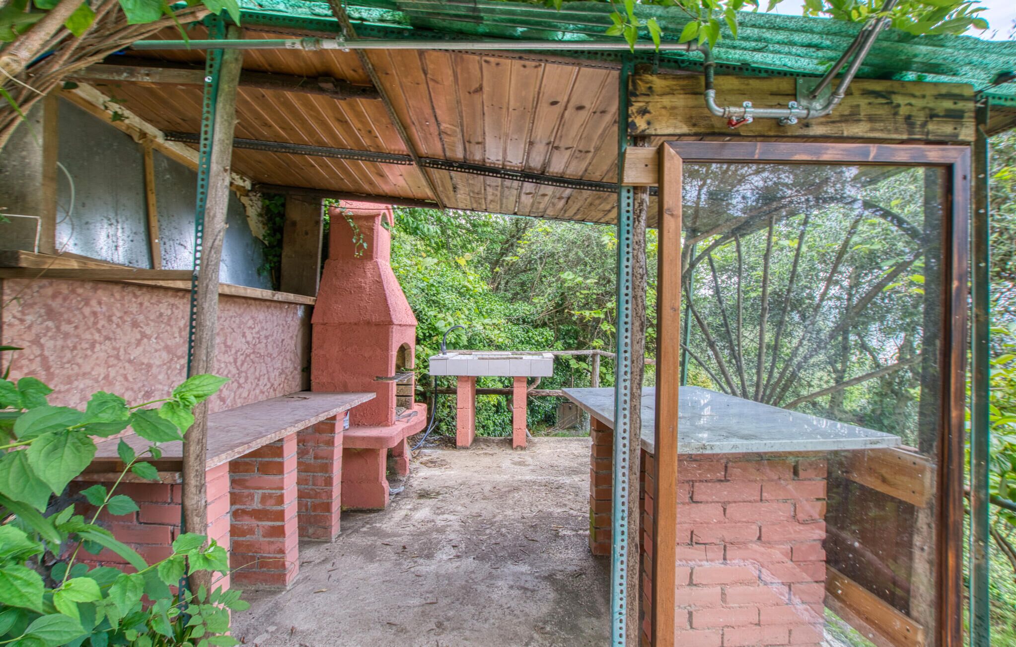 Un espace patio extérieur comprenant un barbecue en briques, une table en bois et une fenêtre à ossature métallique.