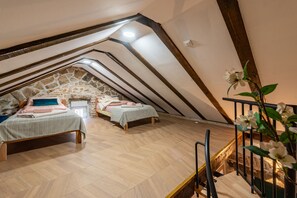 Ein Schlafzimmer im Dachgeschoss mit zwei Betten, einer Steinwand, Holzbalken und einer Treppe.